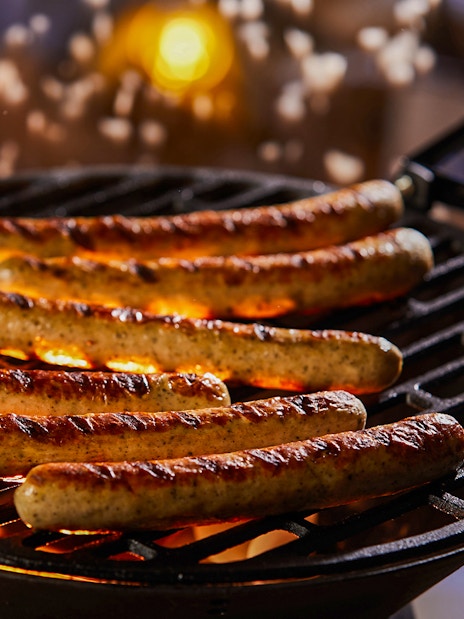 Sausages grilling on barbecue at night with glowing coals.