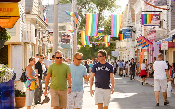 People walking on a colorful street in Provincetown, Cape Cod, with rainbow flags overhead.