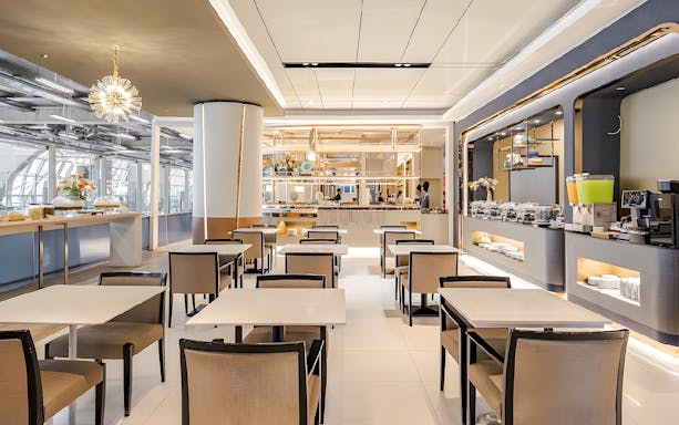 Dining area in Miracle Lounge at Bangkok Airport, featuring tables, chairs, and a buffet setup.