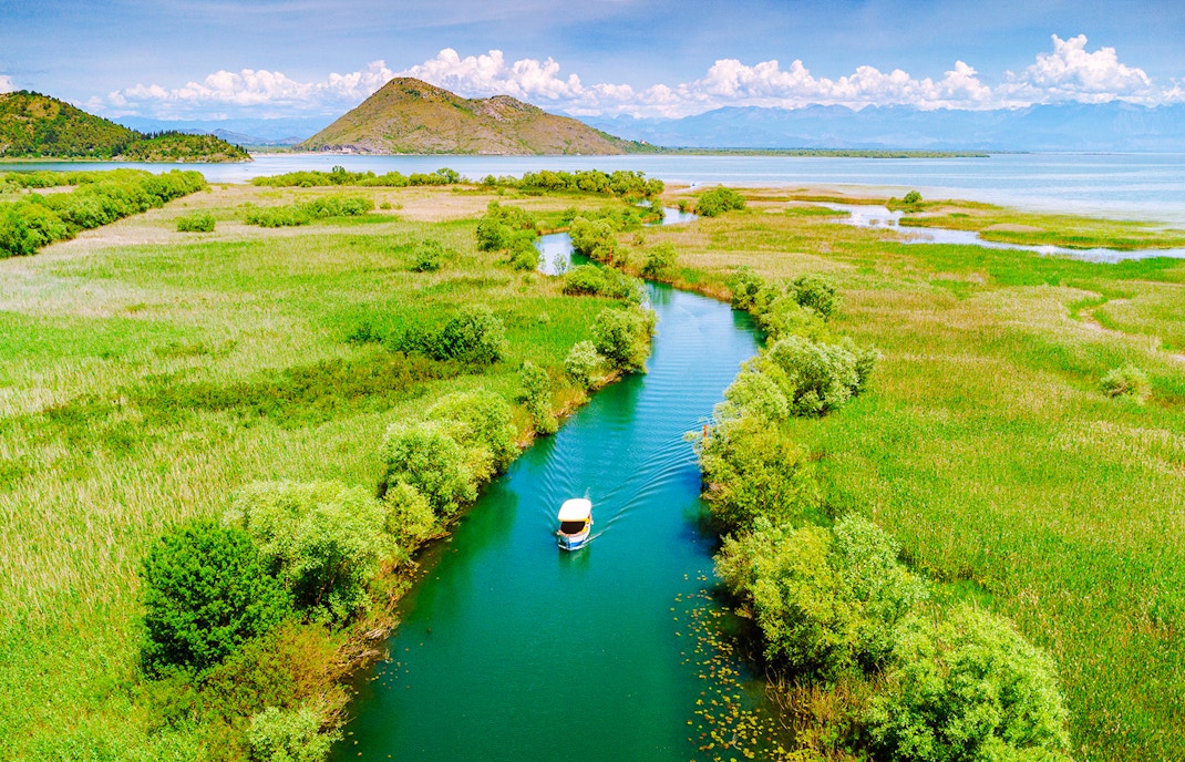 Aerial view of a boat on Lake Skadar, Montenegro, surrounded by lush greenery and calm waters.
