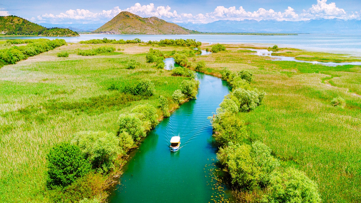 Aerial view of a boat on Lake Skadar, Montenegro, surrounded by lush greenery and calm waters.