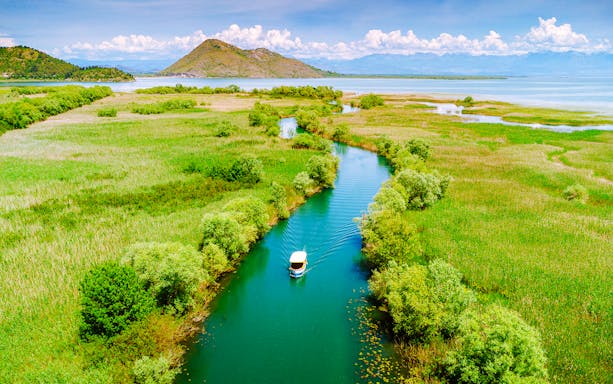 Aerial view of a boat on Lake Skadar, Montenegro, surrounded by lush greenery and calm waters.