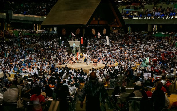 Sumo wrestlers competing in a packed arena during a tournament in Osaka.