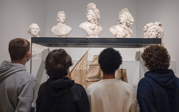 Visitors observing ship model and busts at National Marine Museum, Paris, France.