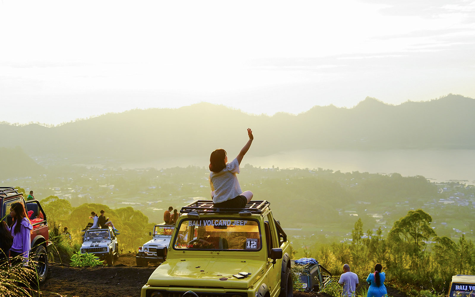 Tourists on Jeep near Mount Batur at sunrise, overlooking scenic landscape in Bali.