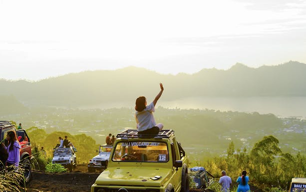 Tourists on Jeep near Mount Batur at sunrise, overlooking scenic landscape in Bali.