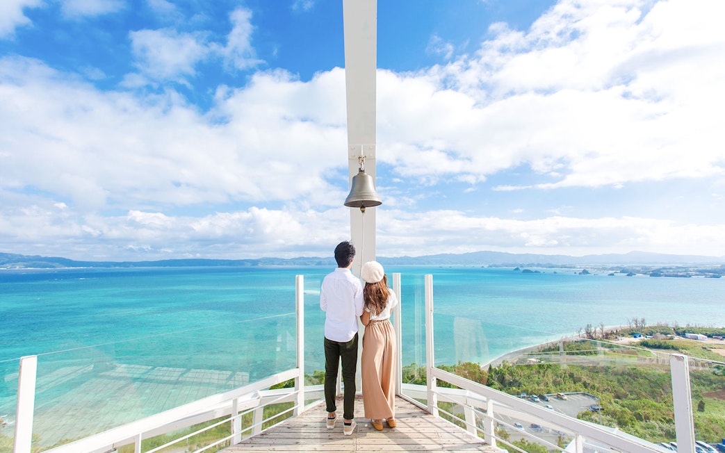 Couple on observation deck with bell overlooking turquoise ocean at Hakone Kowakien Yunessun, Japan.