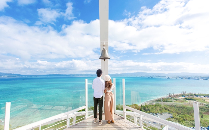 Couple on observation deck with bell overlooking turquoise ocean at Hakone Kowakien Yunessun, Japan.
