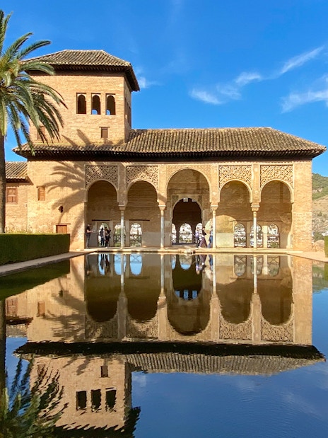 Nasrid Palace reflecting pool with arches and palm trees at Alhambra, Granada.