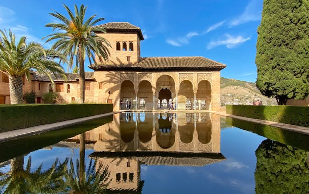 Nasrid Palace reflecting pool with arches and palm trees at Alhambra, Granada.