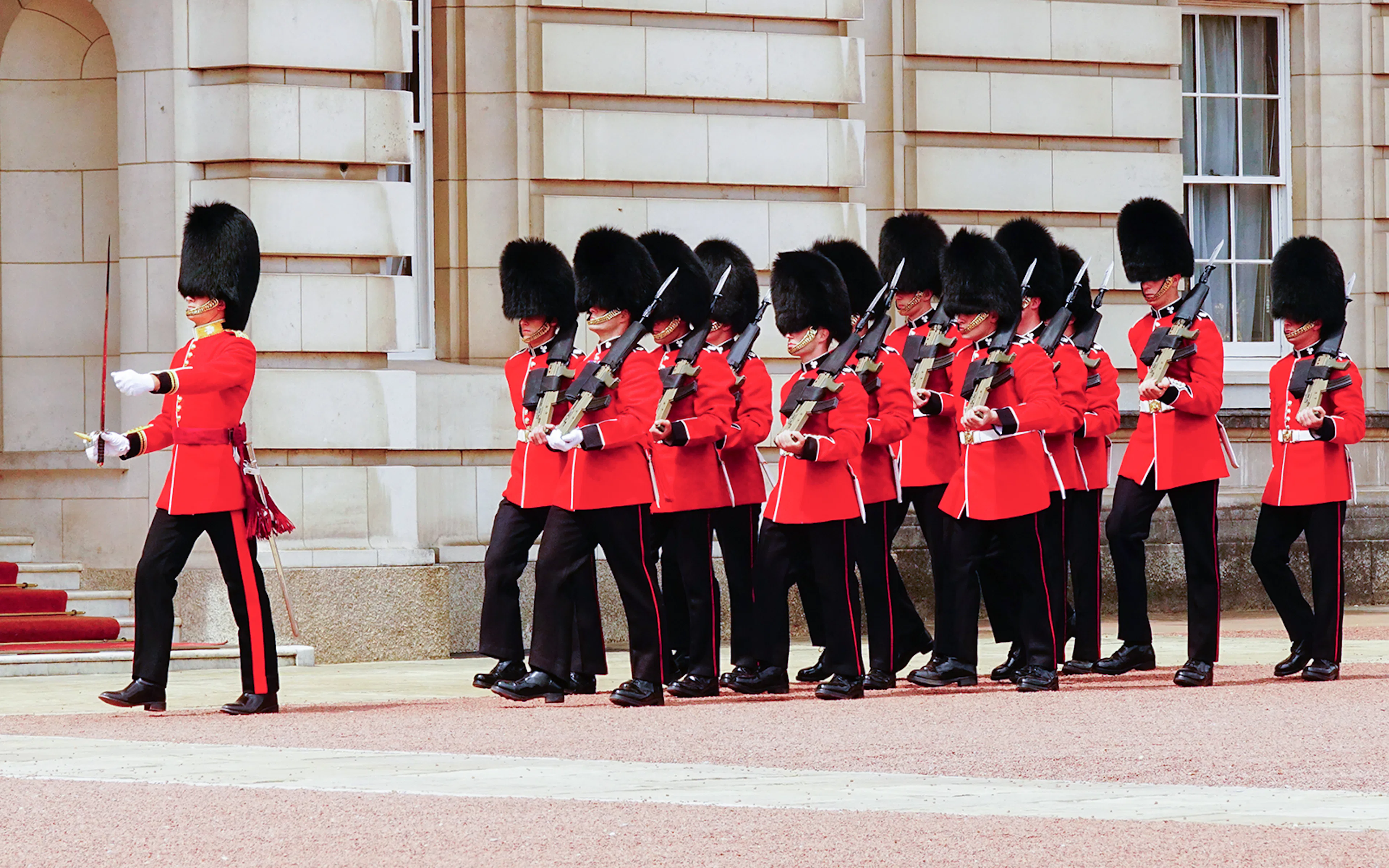 Guards in red uniforms marching at Buckingham Palace, London during the Changing of the Guard ceremony.