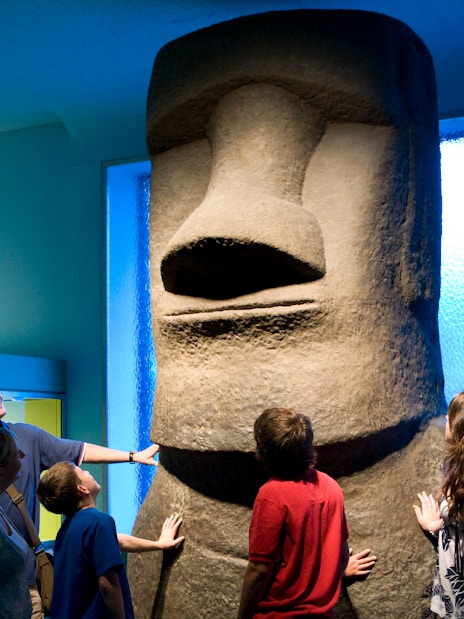 Visitors observing Moai statue at American Museum of Natural History.