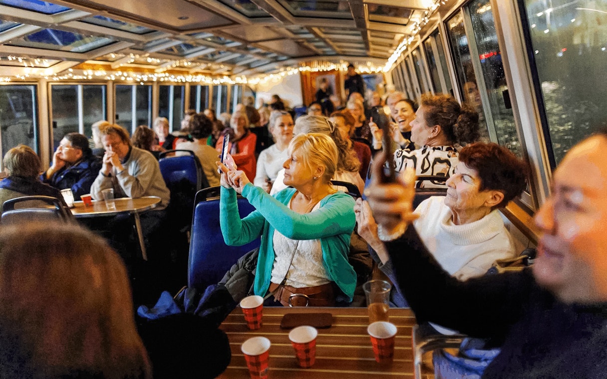 People enjoying the Amsterdam Light Festival cruise, taking photos through the boat's glass roof.