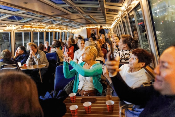 People enjoying the Amsterdam Light Festival cruise, taking photos through the boat's glass roof.