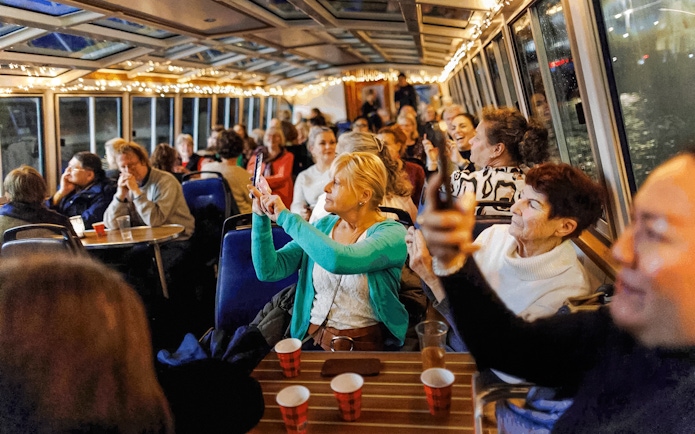 People enjoying the Amsterdam Light Festival cruise, taking photos through the boat's glass roof.