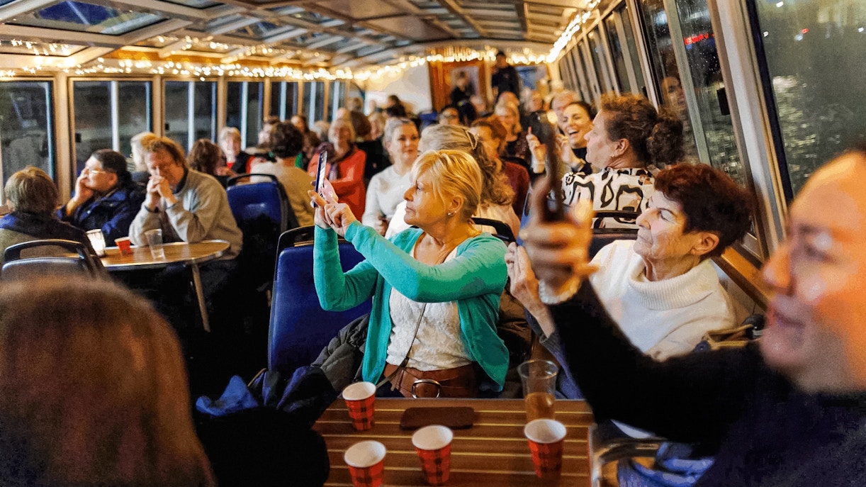 People enjoying the Amsterdam Light Festival cruise, taking photos through the boat's glass roof.