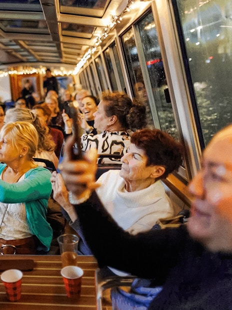 People enjoying the Amsterdam Light Festival cruise, taking photos through the boat's glass roof.