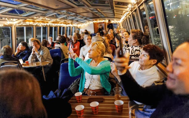 People enjoying the Amsterdam Light Festival cruise, taking photos through the boat's glass roof.