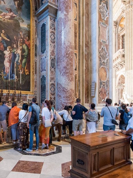 Visitors inside St. Peter's Basilica in Rome viewing artwork and architecture.