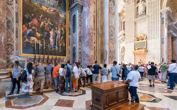 Visitors inside St. Peter's Basilica in Rome viewing artwork and architecture.