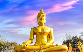 Golden Buddha statue at Wat Phra Yai, Pattaya, under a vibrant sky.