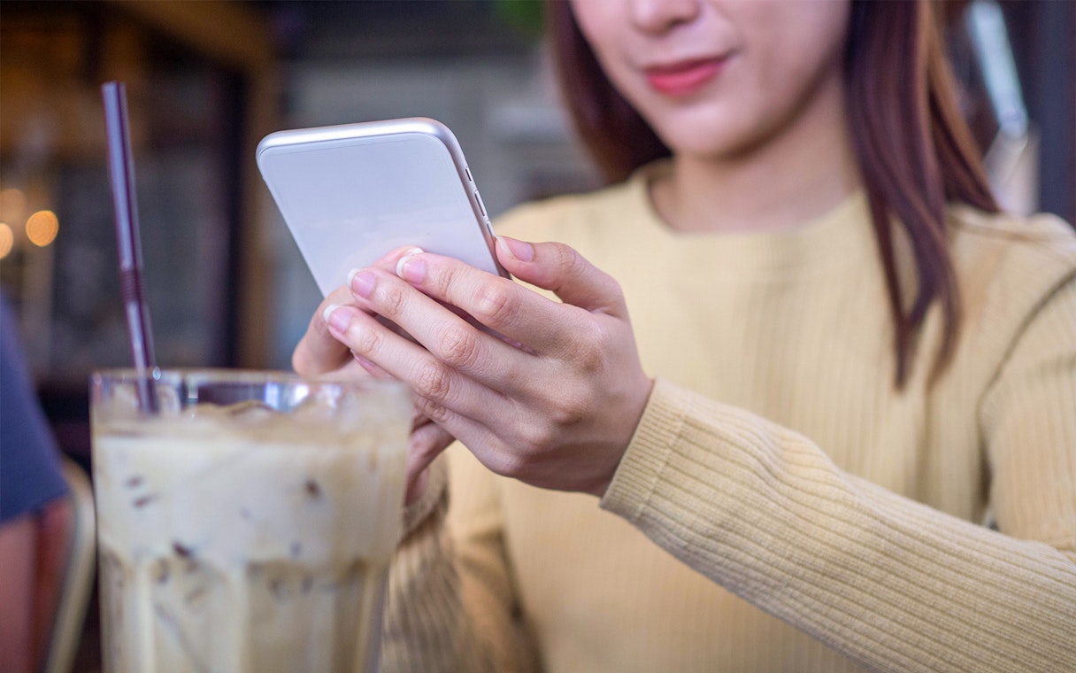 Person using smartphone with Korea Unlimited Data eSIM in a cafe.