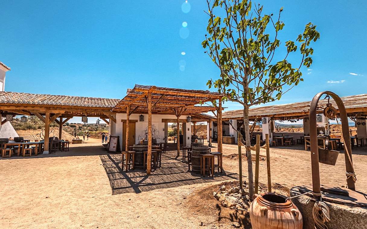 Outdoor dining area at Puy du Fou Park with rustic wooden tables and a tree.