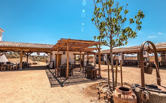 Outdoor dining area at Puy du Fou Park with rustic wooden tables and a tree.