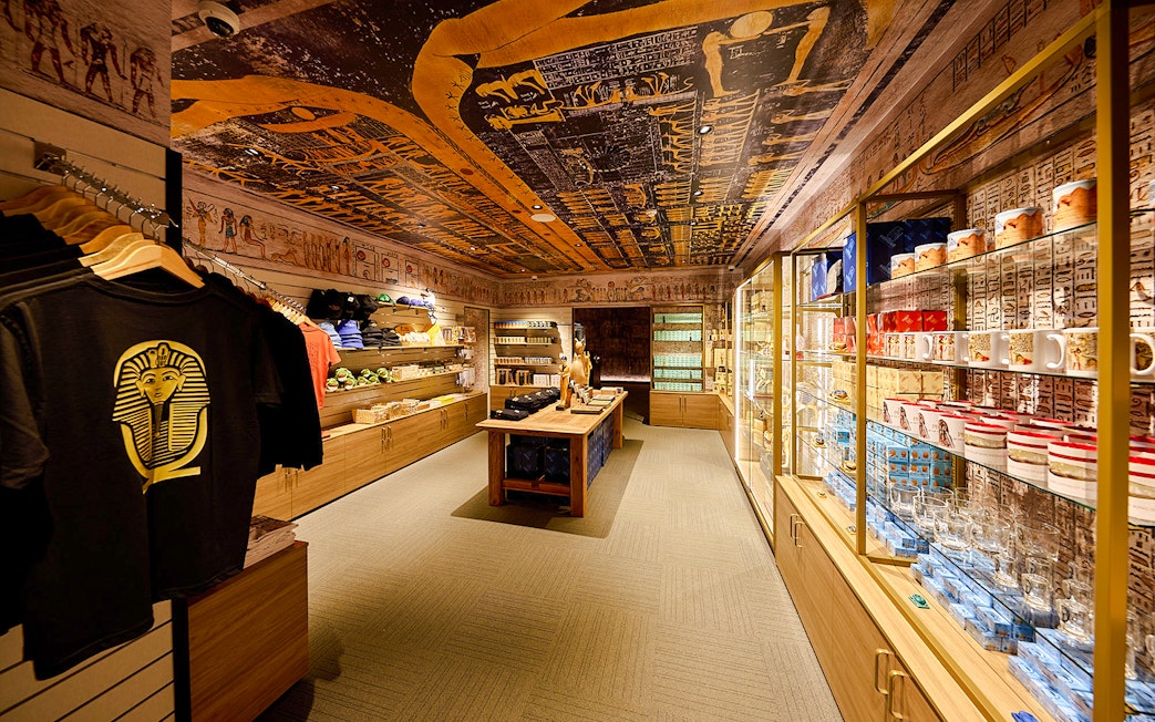 Souvenir shop with Egyptian-themed merchandise and wall art, featuring pharaoh t-shirts and mugs.