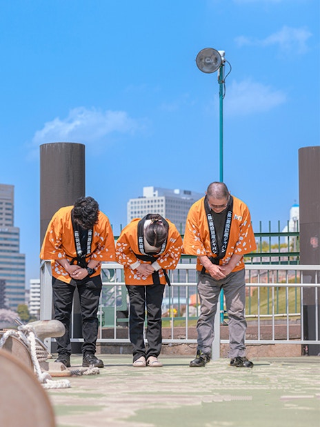 Yakatabune crew in traditional attire bowing on deck with red lanterns in Tokyo.