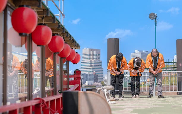 Yakatabune crew in traditional attire bowing on deck with red lanterns in Tokyo.