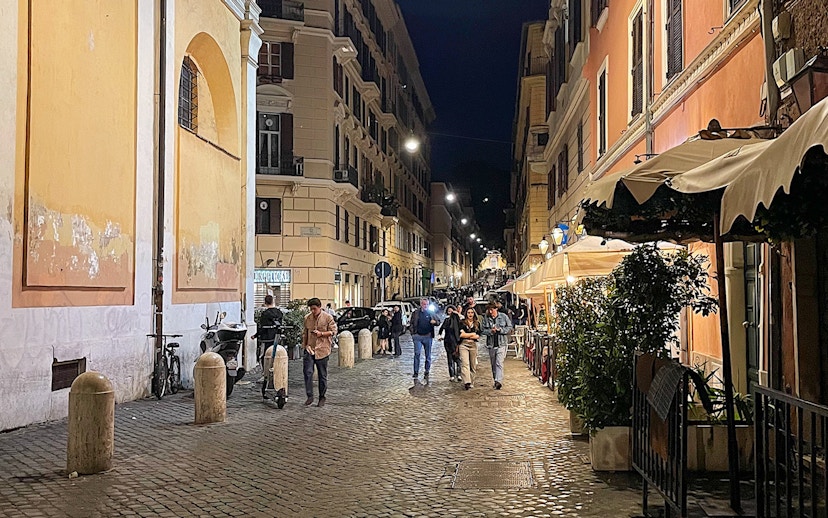 Cobblestone street in Rome at night with people walking and outdoor cafes.