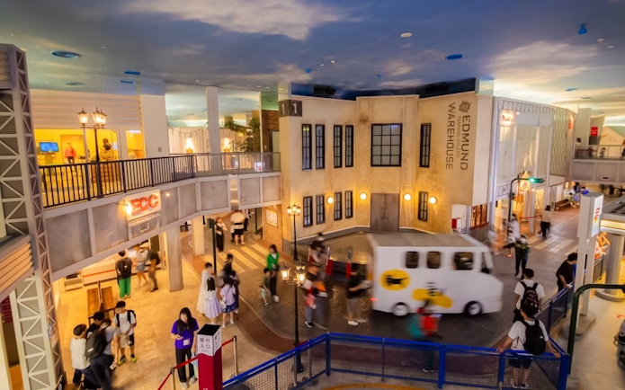 Street view of KidZania Osaka Koshien with children exploring and a small vehicle passing by.