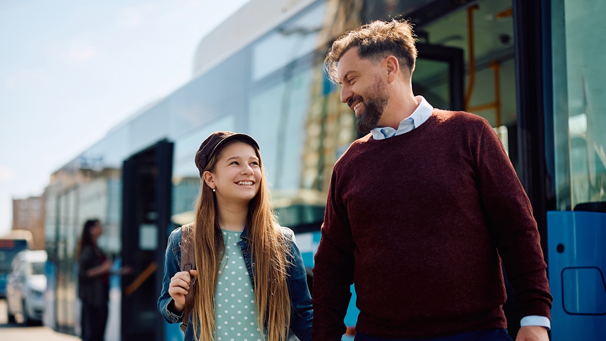 Kid and parent smiling while exiting a bus.