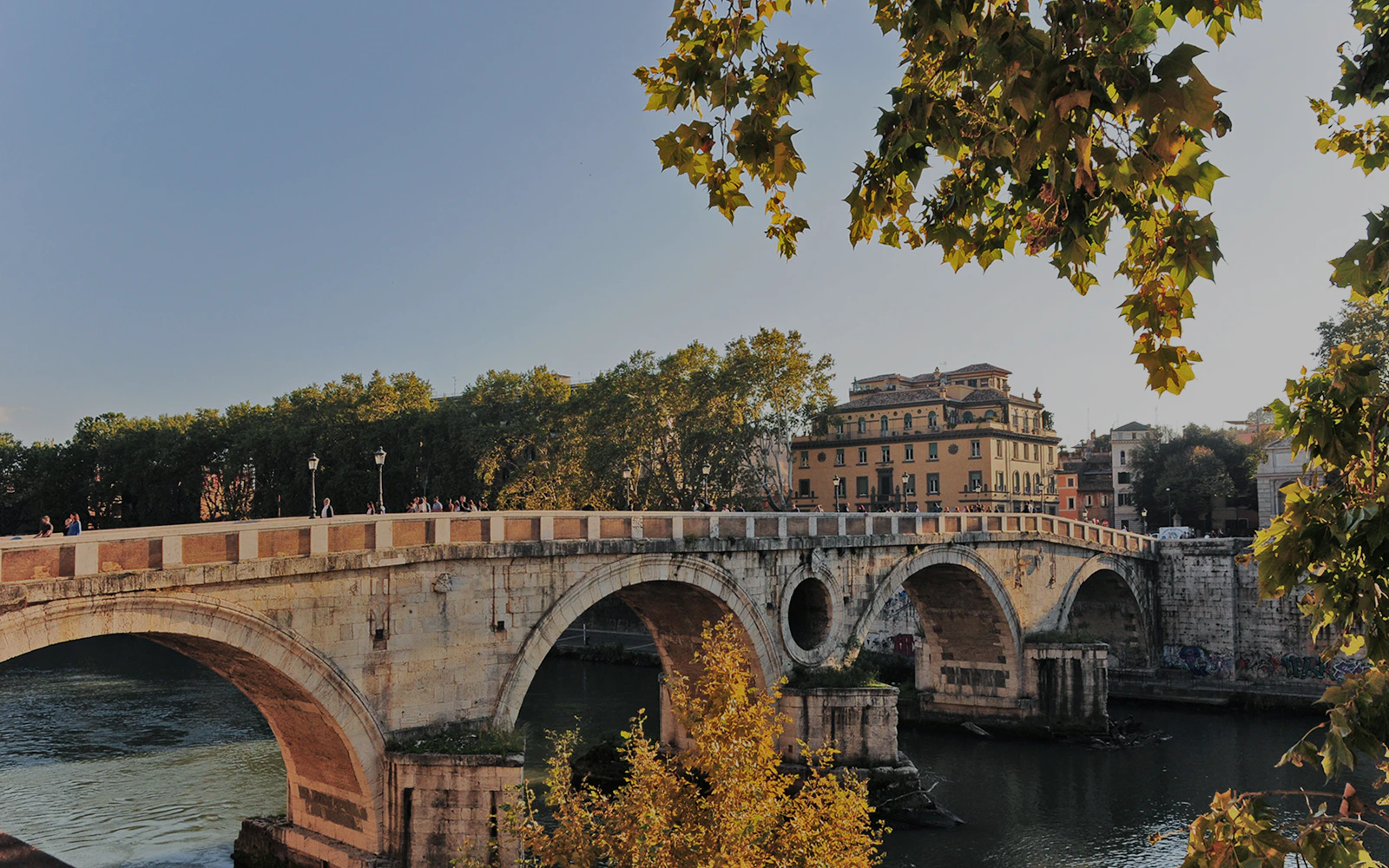 Ponte Sisto bridge over the Tiber River in Rome with trees and buildings in the background.
