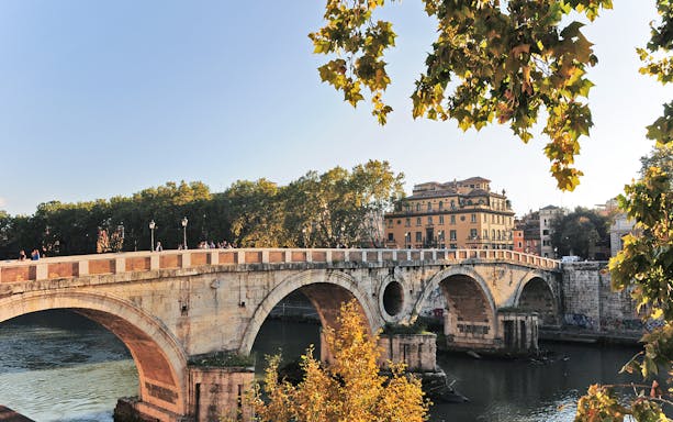 Ponte Sisto bridge over the Tiber River in Rome with trees and buildings in the background.