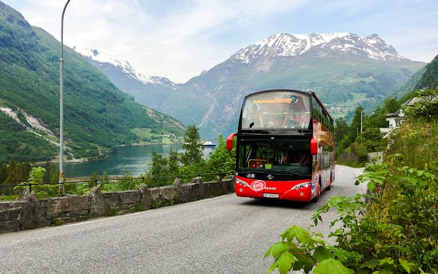 Red double-decker bus on Geiranger Hop-on Hop-off tour with fjord and mountains in Norway.