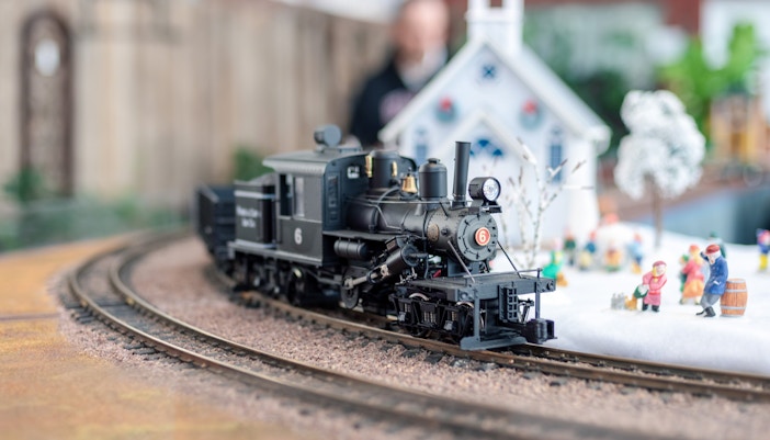 Model train on snowy track with miniature figures and a church, Holiday Train Show.
