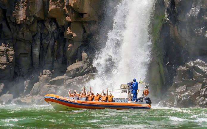 Tourists on a boat near Iguazú Falls, Brazilian side, with waterfall in background.