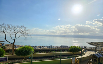 Private 4-star resort view of the Dead Sea, Jordan, with sunlit water and landscaped gardens.