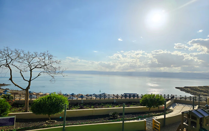 Private 4-star resort view of the Dead Sea, Jordan, with sunlit water and landscaped gardens.