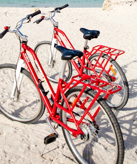 Red bicycles on sandy beach with ocean in background, Rottnest Island, Western Australia.