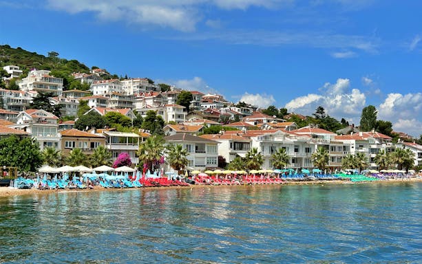 Seaside view of Princes' Islands with beach chairs and umbrellas, showcasing coastal houses.