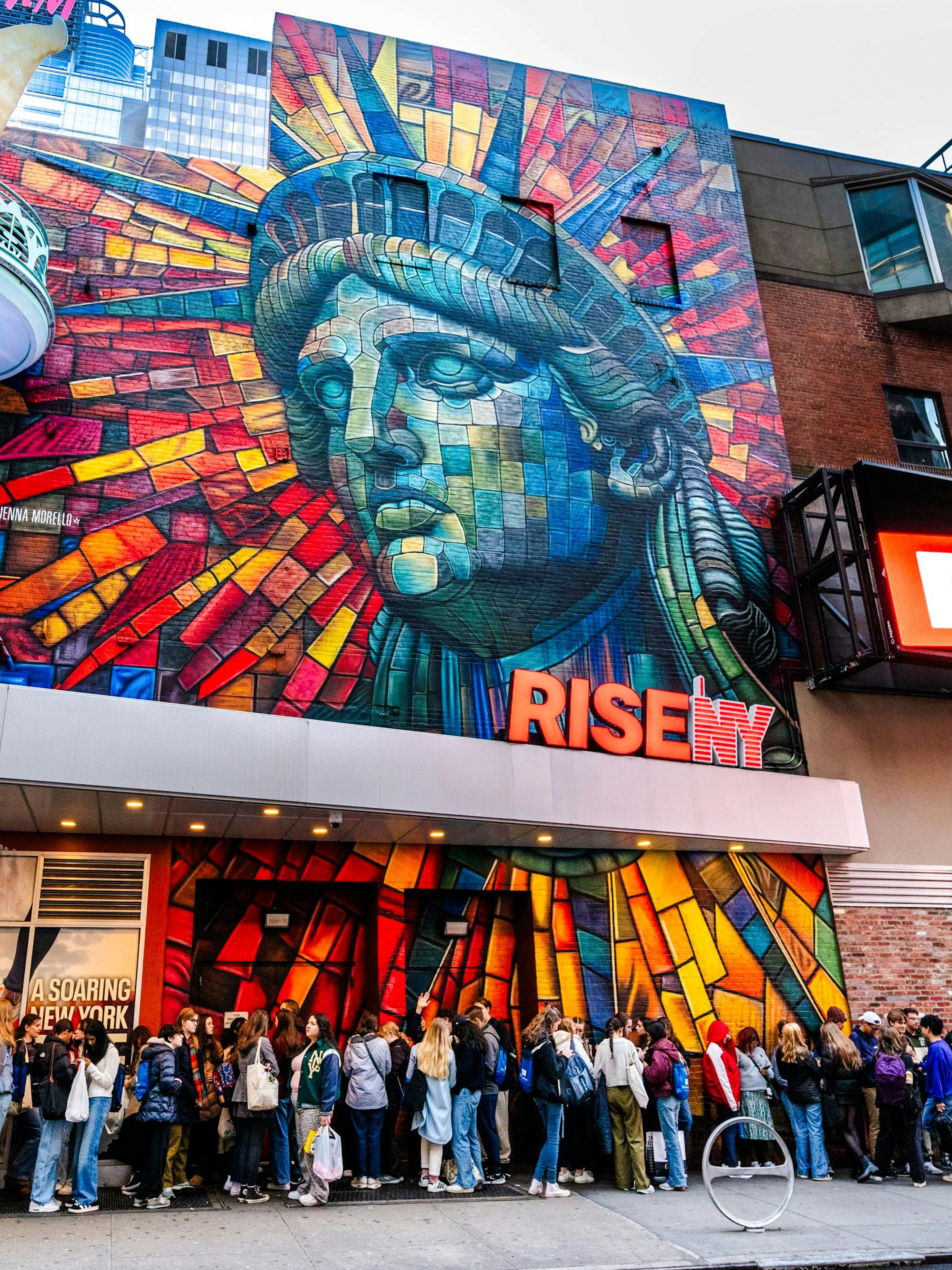 Exterior mural of Rise NY with Statue of Liberty mosaic and people in line, New York City.