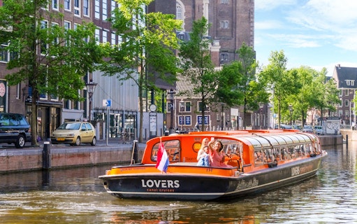 Canal cruise boat on Amsterdam canal with passengers taking photos.