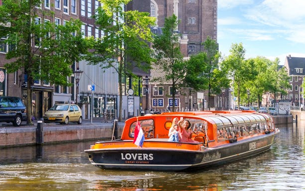 Canal cruise boat on Amsterdam canal with passengers taking photos.