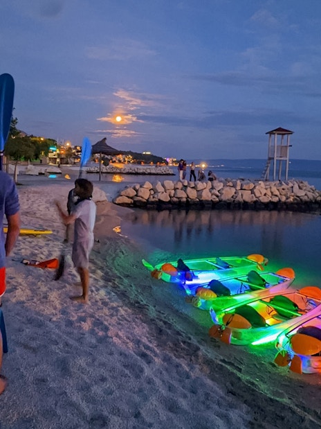 Group preparing for SUP Glow Tour in Split with illuminated kayaks on the beach at dusk.