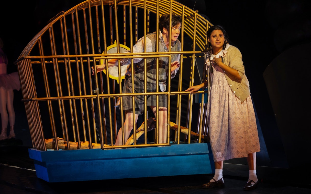 Hansel and Gretel stage performance with characters near a large cage.
