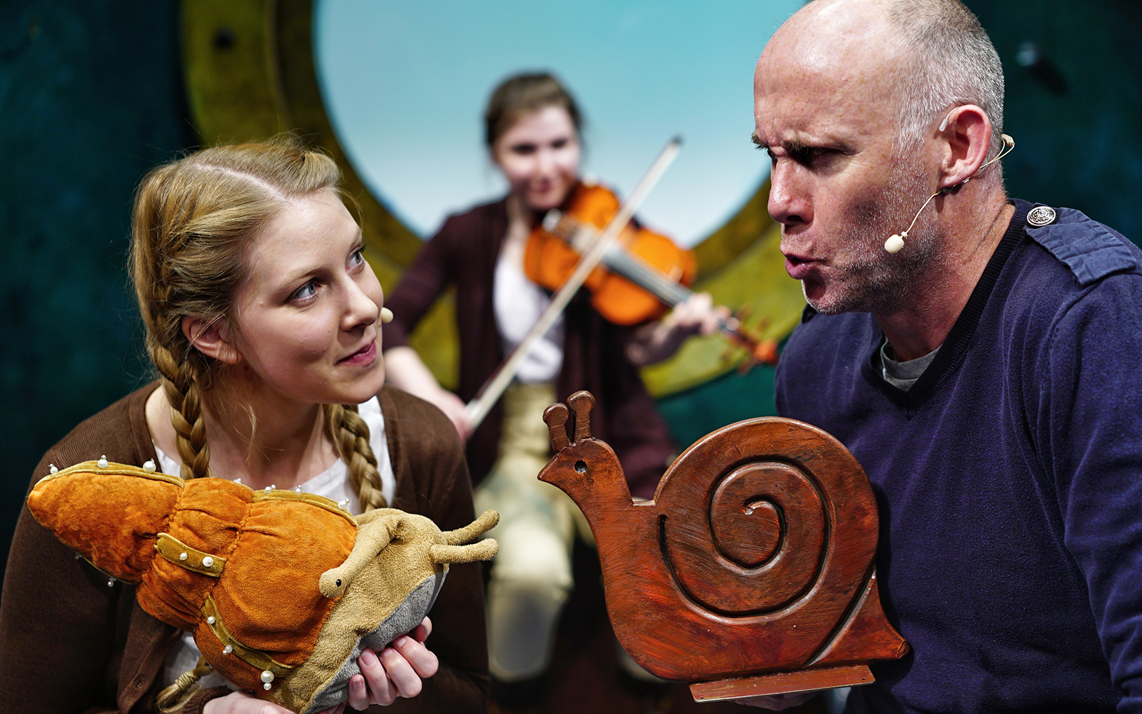 Actors performing "The Snail and the Whale" with puppets and violinist in background.
