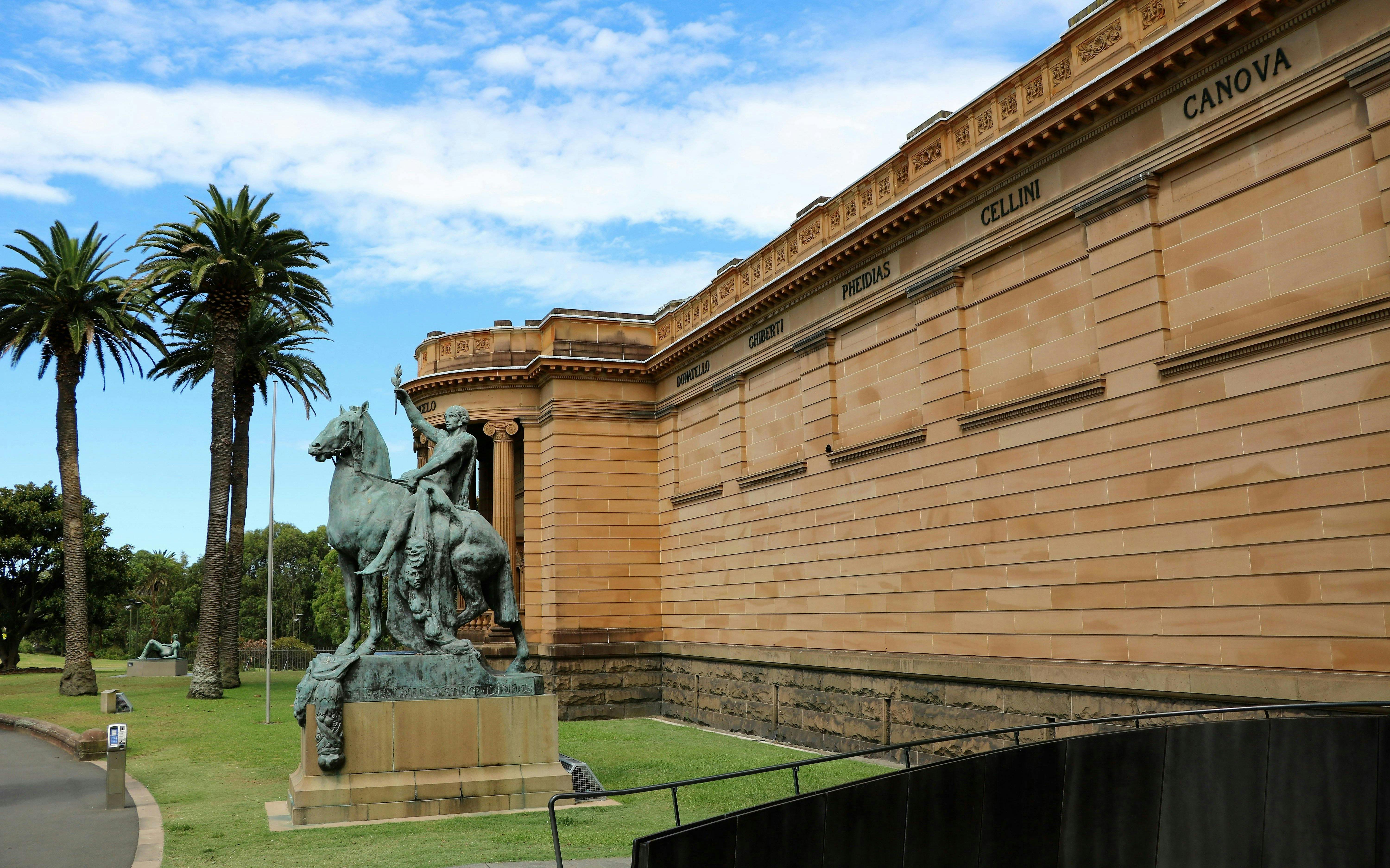 Statue outside Art Gallery of New South Wales, Sydney, with palm trees and classical architecture.